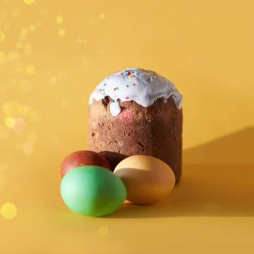 Close-up of colored Easter eggs and a cake on a yellow background with a golden Stock Photos