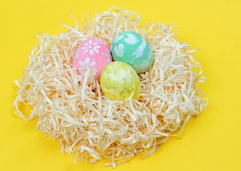 Close up of colored Easter eggs in nest on a yellow background Stock Photos