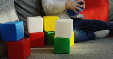 Close up of the colourful kid's cubes on the grey couch and kid's hands playing Stock Footage 82916470