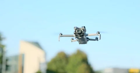 Close-up of a compact camera drone hovering in flight against a blue sky Stock Footage 343928035