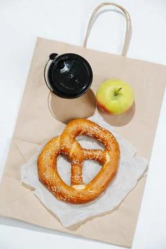 Close up composition of a cup of coffee, pretzel and an apple on a paper bag Foto stock