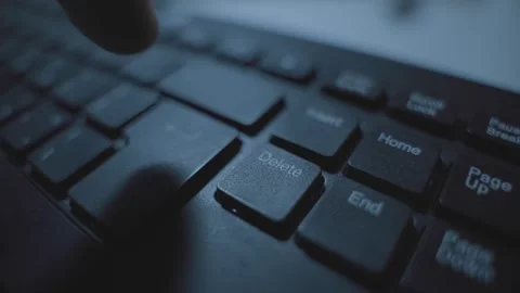 Close up on computer keyboard as hand presses delete keypad in dark room Video stock 332648441