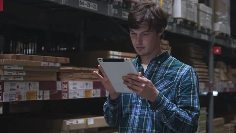 Close up. Concentrated young brunette guy employee with tablet checking goods in Stock Footage 154138033