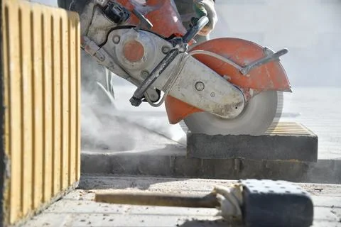 Close-up of concrete block, worker cutting road curb with circular saw. 스톡 사진