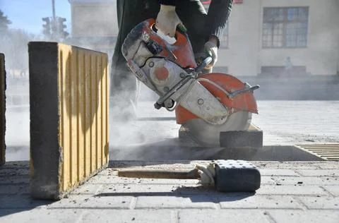 Close-up of concrete block, worker cutting road curb with circular saw. Stock Photos