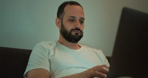 Close up of a confident brunette guy with a beard in a white T-shirt sitting on Stock Footage 280654376