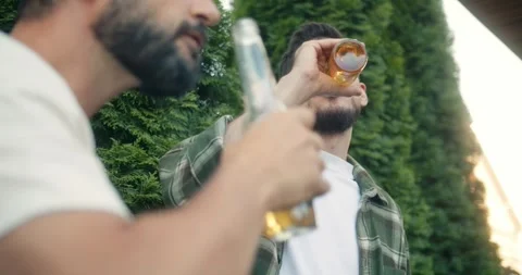 Up close confident brunette guy with a beard clinks a bottle of beer and drinks Stock Footage 283830681