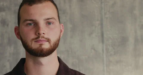 Close-up of a confident, calm man looking into the camera against a gray wall. A 스톡 동영상 347012074