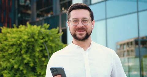 Close-up of a confident Caucasian man using a smartphone, looking at camera, sta Stock Footage 333699406