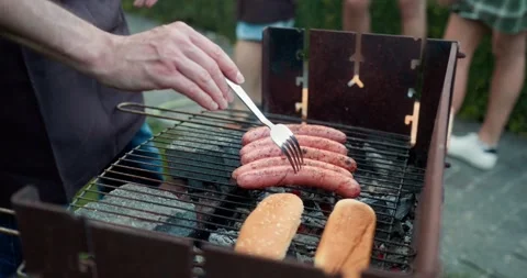 Close up of a confident guy in a black apron warming up sausages and buns for a Stock Footage 283832230