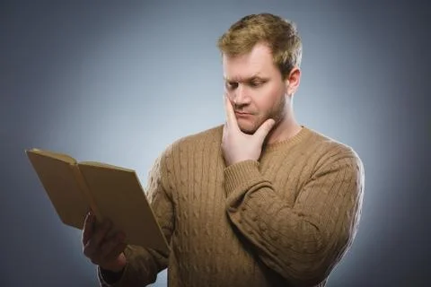 Close-up of confused man reading book against gray background Stock Photos