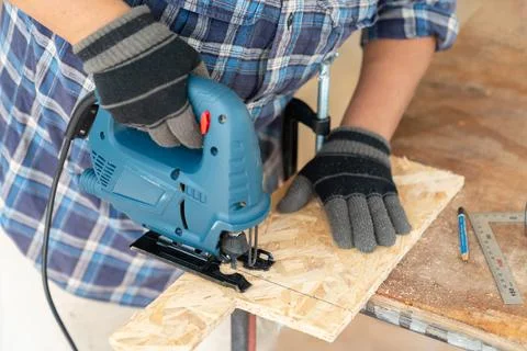 Close up construction worker hands using electric jig saw for cutting wooden Stock Photos