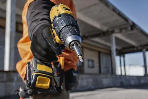 Close up of construction worker holding cordless drill at building site. Co.. Stock Photos