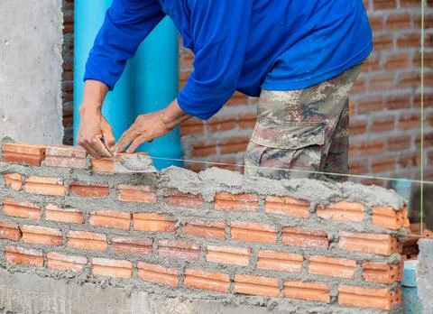 Close-up of a construction worker using a trowel to lay red clay bricks wit.. Stock Photos