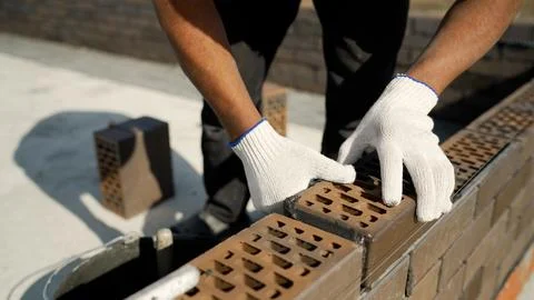 A close-up of construction workers carefully laying bricks for a new wall, hi Stock Photos