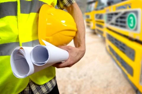 Close up of a construction worker's hand holding project documents and hat. Stock Photos