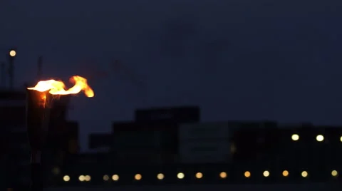 Close up of a container ship at night on a river and a fire torch in front Stock Footage 67676416