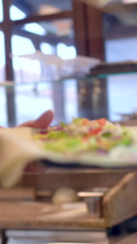 Close-up of cook assembling flatbread wrap with lettuce and purple cabbage on Видео 336534394