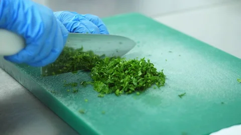 Close-up, a cook in blue gloves cuts greens, parsley on the kitchen board Stock Footage 103577363