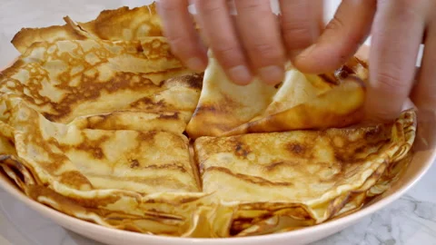 Close-up of a cook placing a folded thin pancake, crepe, on a plate. Stock Footage 305386295