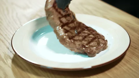 Close-up of a cook puts freshly cooked meat steak on a plate. Stock Footage 88572277