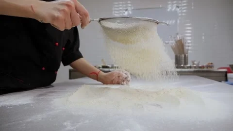 Close-up of the cook sifting flour on the kitchen table, slow motion. Stock Footage 136846238