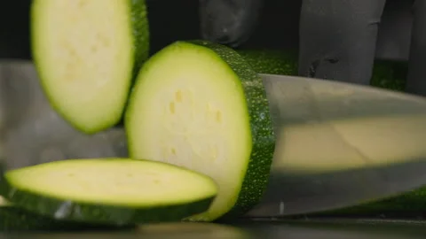 Close-up of a cook slicing a courgette. He uses a knife and cuts on a black Stock Footage 163045310