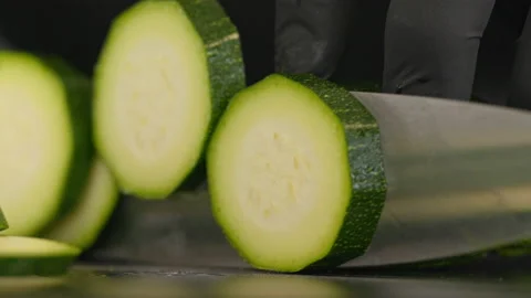 Close-up of a cook slicing a courgette. He uses a knife and cuts on a black Stock Footage 163045659