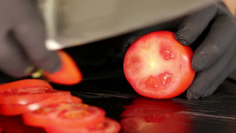 Close-up of a cook slicing a tomato. He uses a knife and cuts on a black board. Stock Footage 163046809