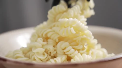 Close-up of cooked fusilli pasta added to bowl with pasta server Stock Footage 348645992