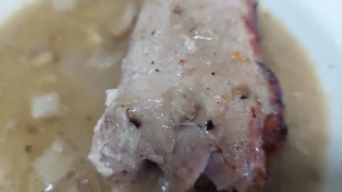 Close-up of cooked meat with thick onion gravy sauce on a plate Stock Footage 336460632