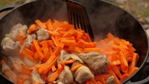 Close-up of cooking a dish with meat and carrots in a cast-iron cauldron. Stock Footage 294354874
