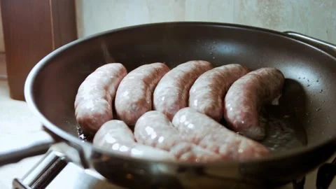 Close-up of cooking sausages in black pan with oil. Frying sausages in hot Stock Footage 144321959