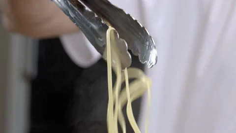 A close-up of the cook's hands lifting boiled steamed spaghetti pasta with tongs Stock Footage 275246857