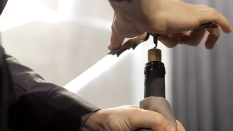 A close-up of a corkscrew twisting into a bottle of red wine. A waiter opens a Stock Footage 167242254