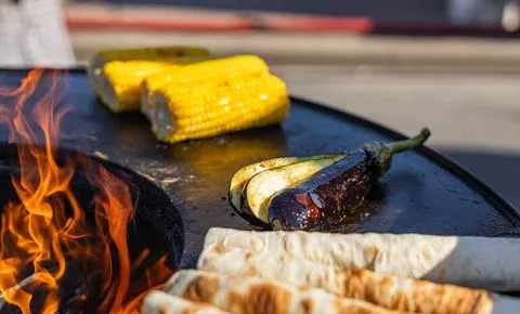 Close-up of corn and meat grilling on a barbecue. The corn is charred and gol Stock Photos