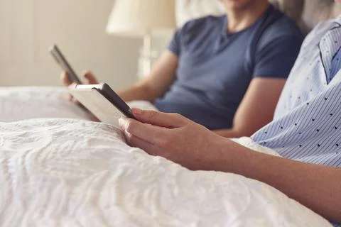 Close Up Of Couple At Home In Bed Using Digital Tablet And Mobile Phone During Stock Photos