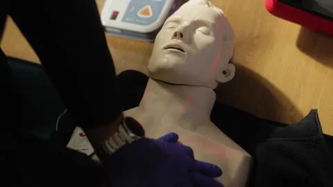 Close-up of a CPR training session using a mannequin on a wooden floor. The Stock Footage 292680733