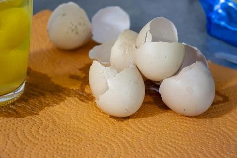 A close-up of cracked eggshells scattered on an orange paper towel, with a glass Stock Photos
