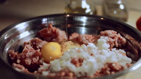 Close-up of cracking egg above minced meat in metallic bowl. Process of Stock Footage 144822332
