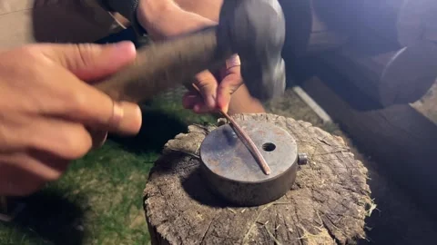 Close-Up of Craftsman Hammering Copper Wire on Anvil Mounted on Wooden Log Stock Footage 345522302