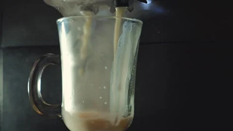 Close-up of a creamy coffee beverage pouring from a machine into a glass mug Stock Footage 346472010