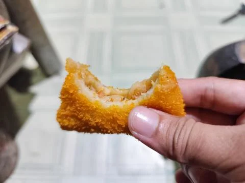 Close Up of Crispy Breaded Fried Snack Held by Hand Showing Layered Filling Stock Photos