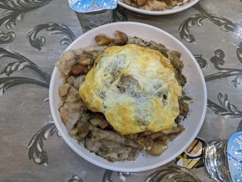 Close-up of crispy fried egg over savory chicken dish on patterned tablecloth Stock Photos