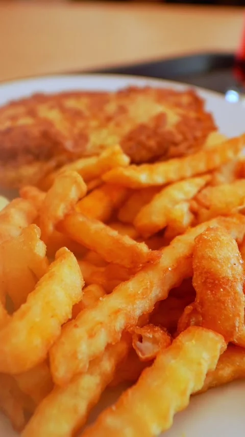 Close-up of crispy golden fries with a breaded schnitzel in the background Stockbeeldmateriaal 333651075