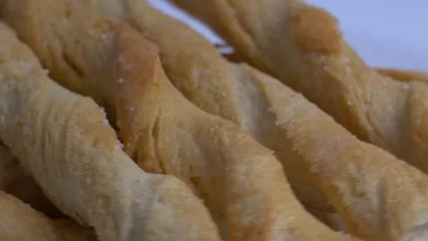 Close-up of crispy twisted puff pastry breadsticks rotating on a white plat.. Stock Footage 340070865