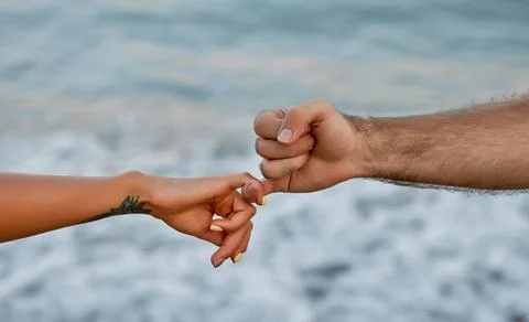 Close-up cropped image of a young couple's hands in front of the sea and wave Stock Photos