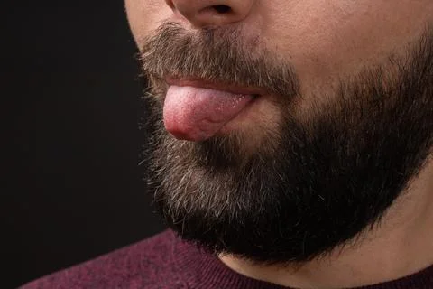 Close-up of cropped portrait of young bearded man showing tongue out, isolated Stock Photos