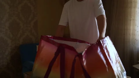 Close-up cropped shot of unrecognizable man packing clothes into large colorful Stock Footage 294259432