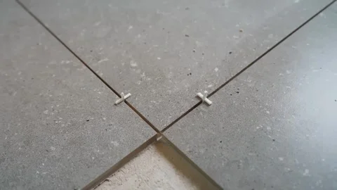 Close-up of cross spacers aligning gray floor tiles around an unfinished Stock Footage 345833909